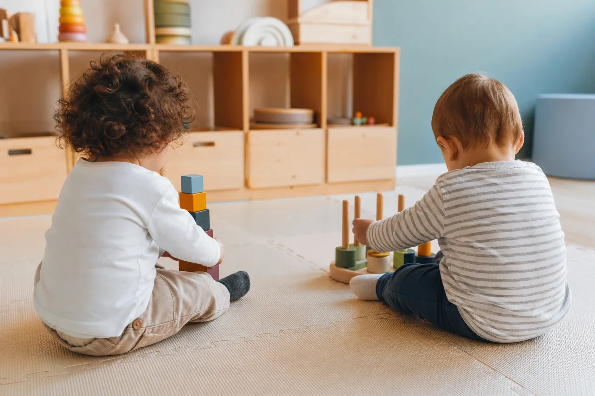 Deux jeunes enfants installés côte à côte sur un tapis de crèche, chacun absorbé par son propre jeu de construction